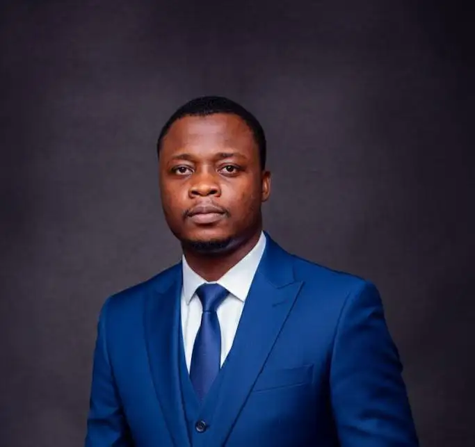 Professional portrait of a man wearing a blue suit and tie against a dark studio background.