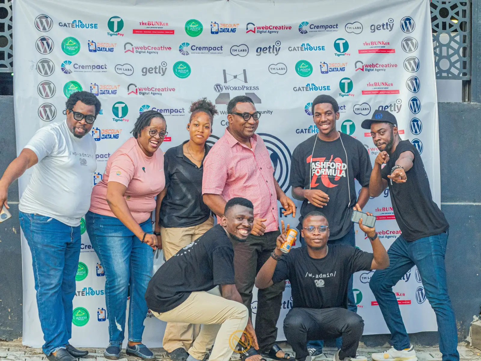 WordPress community members posing together in front of an event sponsor backdrop during a community event.